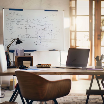 Modern Home Office with Whiteboard and Sunlight - A cozy and modern home office setup featuring a wooden desk, a laptop, and a whiteboard covered with notes. Sunlight streams through the large windows, creating a warm and productive environment.