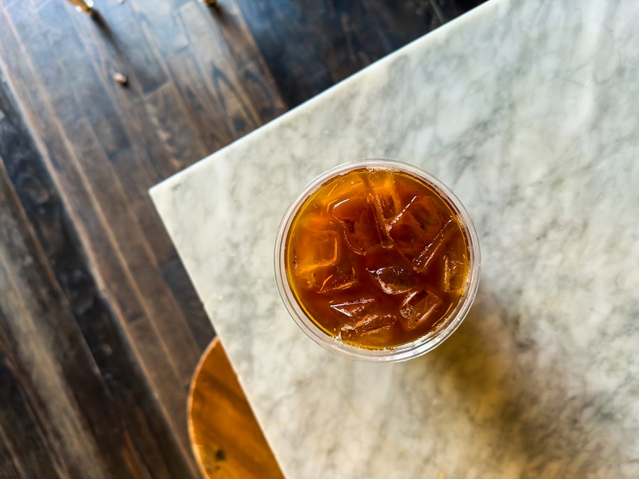 Photo: A focused glass of iced coffee on a marble table in a coffee shop with blurred background