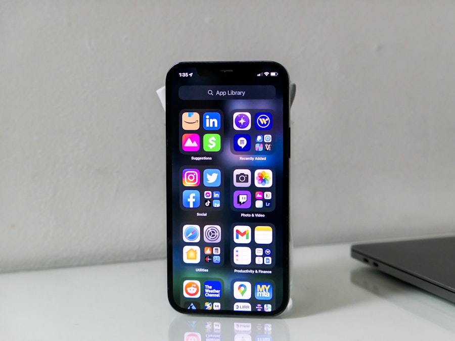 Photo: A smartphne with a lit screen showing app icons on a white glass desk surface 