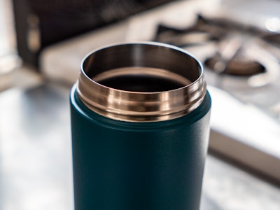 Steel Coffee Tumbler - A close up of a metal blue and silver coffee cup with a blurred background 