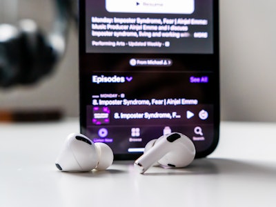 Earbuds with Phone with Podcast - A smartphone with earbuds on a white desk