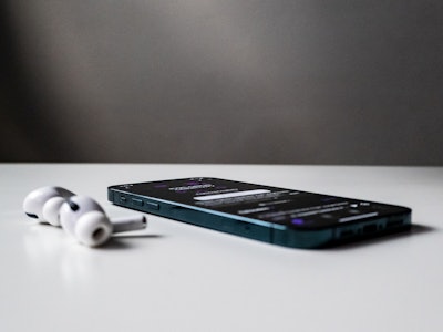 Earbuds with Phone on a Desk Playing a Podcast - A smartphone and earbuds on a white table