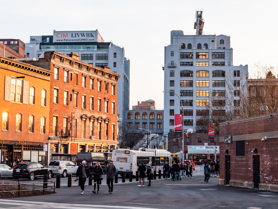 Photo: A group of people on a city street standing in front of a bus and cars