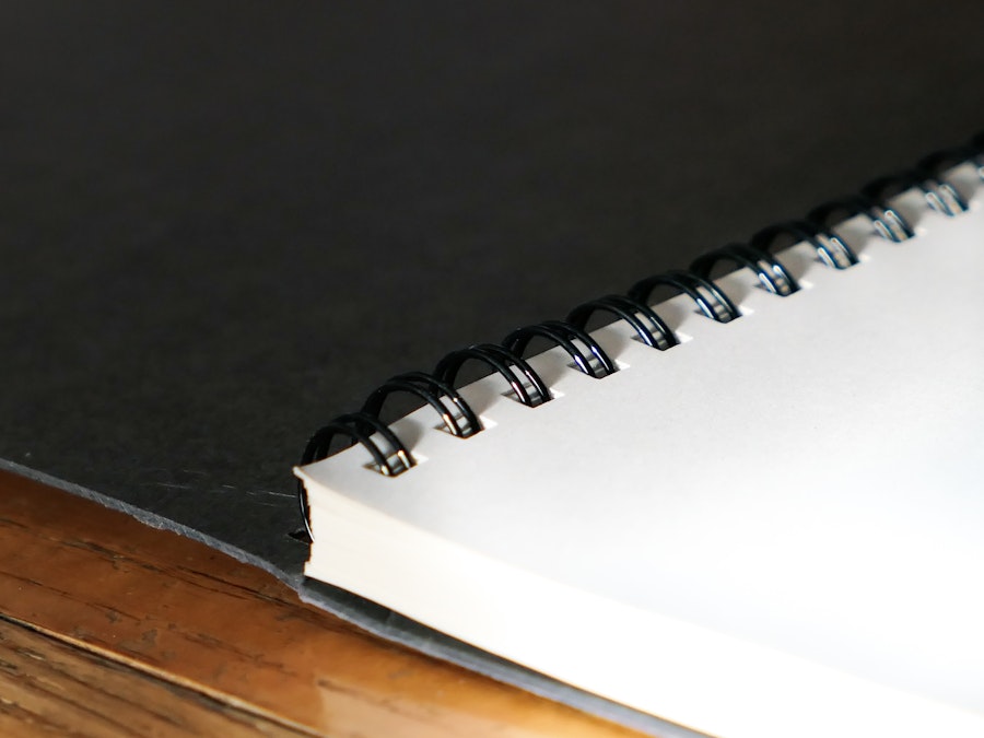 Photo: A spiral bound notebook with a black cover on a wooden desk 