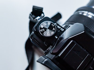 Black Mirrorless Camera on White Desk - A close up of a black camera with dials on a white desk