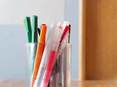 Pens and Markers - A group of pens, markers, pencils, and highlighters in a cup on top of a wooden desk
