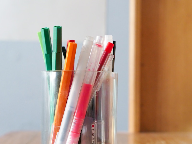 Photo: A group of pens, markers, pencils, and highlighters in a cup on top of a wooden desk
