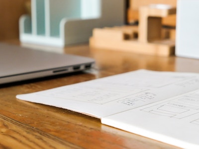 Laptop and Notebook on Desk - A notebook in focus and a blurred laptop on a wooden desk