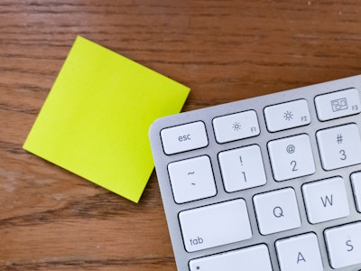 Keyboard on Desk - A keyboard on top of a yellow stack of post-it notes with a wooden desk background 