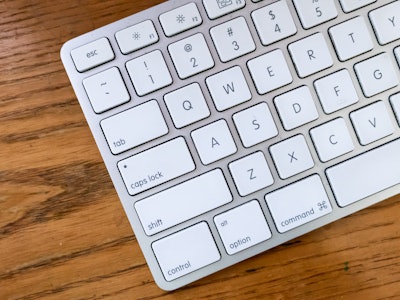 Keyboard on Wood Desk - A metal gray and white keyboard on a wooden desk