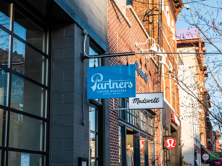 Photo: Signs for coffee shops and retail stores hanging from buildings on a city street