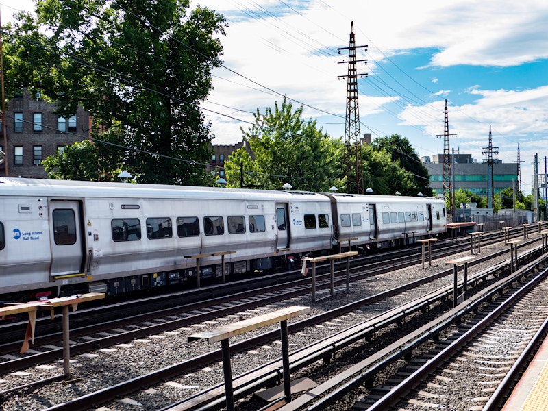 Photo: A train on the tracks with other empty tracks next to it surrounded by trees and buildings