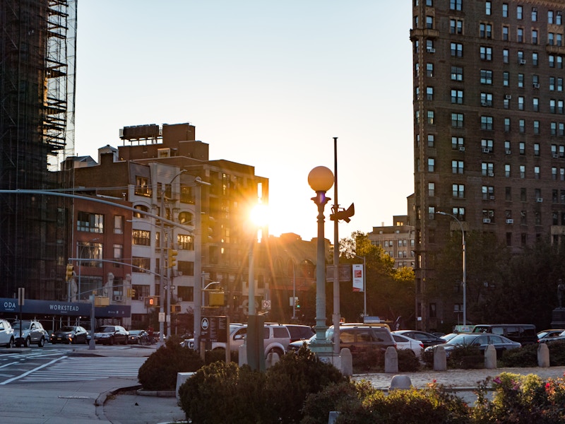 Photo: A sun shining through the sky on a city street with buildings and cars