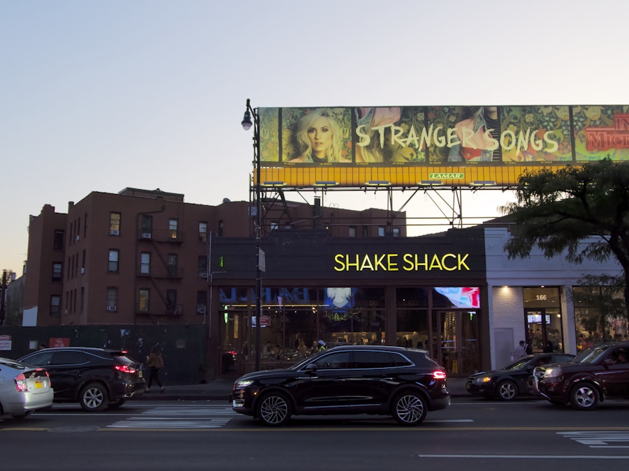 Photo: A car parked on the side of the road in front of storefronts, billboards, and apartments 