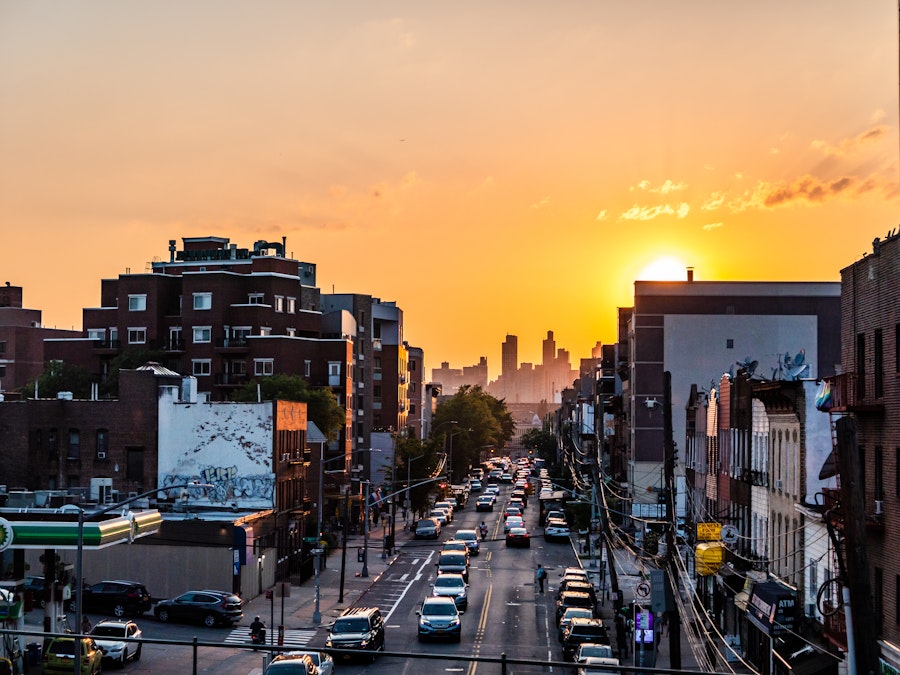 Photo: A city street with cars and buildings with the sunset in the distance 