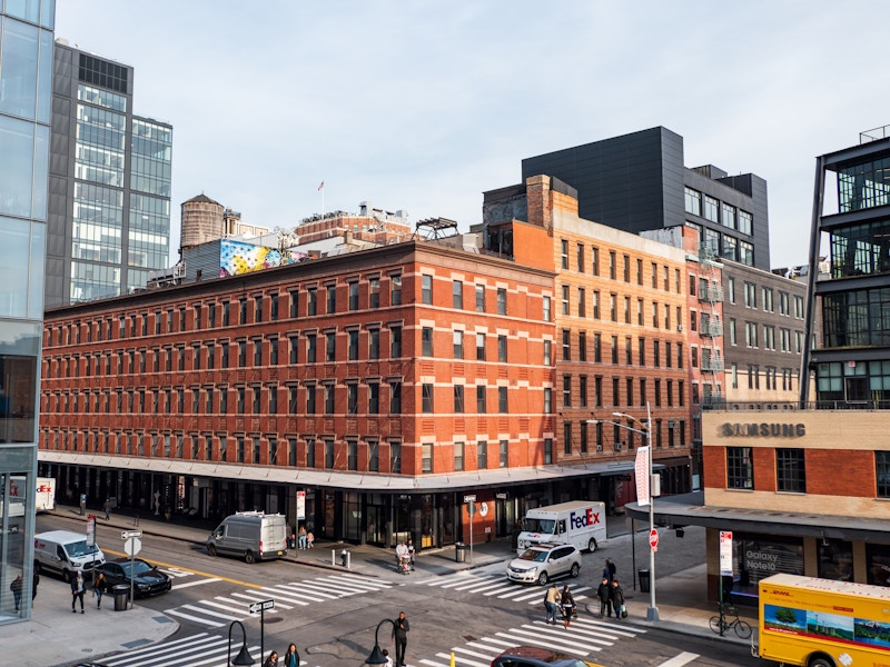 Photo: A large building with many windows on a city street with cars parked and people walking 