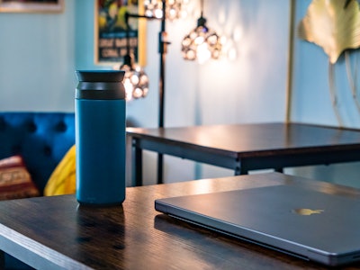 Tumbler and Laptop on Table In Coffee Shop - A black and blue tumbler on a wooden table with a laptop at a coffee shop. 
