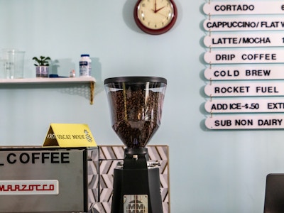 Bean Grinder and Menu in Coffee Shop - A coffee machine with beans in it and menu board at a coffee shop