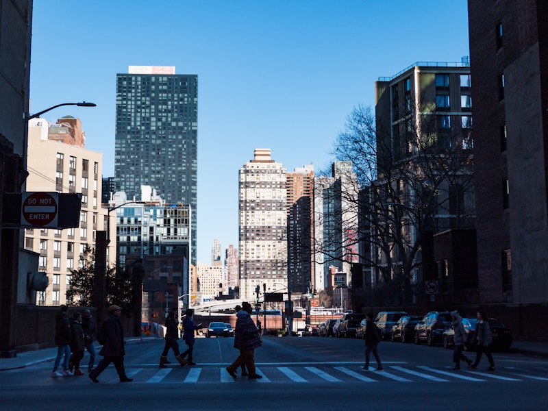 Photo: Silhouetted people walking on a street in a city with buildings in the background 