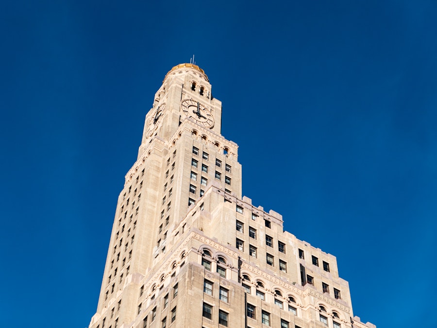 Photo: Looking up at a tall building with a clock on top under blue sky 