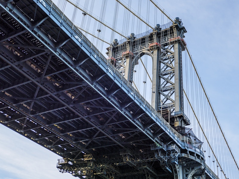 Photo: Looking up at a bridge with many wires under blue sky