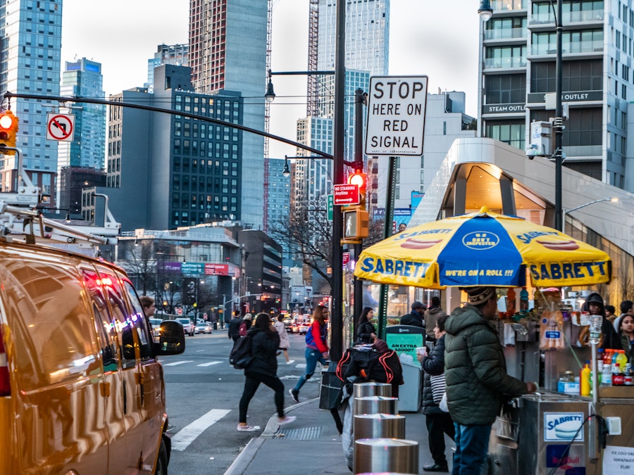 Photo: A city street with a food stand and people crossing the street