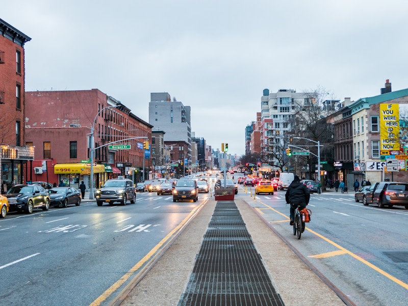 Photo: A city street with cars and people on it with buildings around it