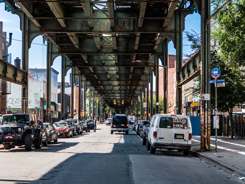 Photo: Cars parked on a street under train tracks 