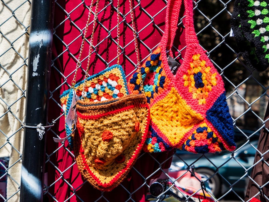 Photo: A group of colorful knitted bags on a fence at an artist market 