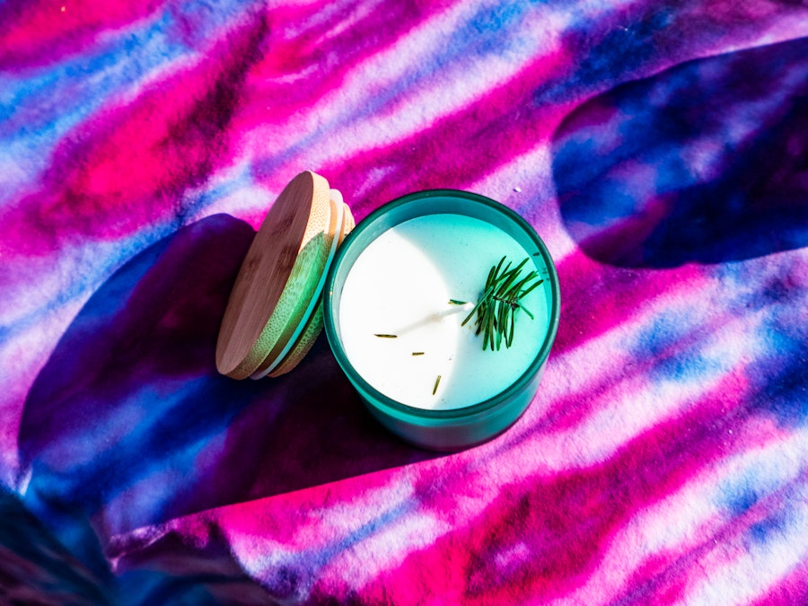 Photo: A candle with a sprig of rosemary on a pink and purple blanket at an artist market 