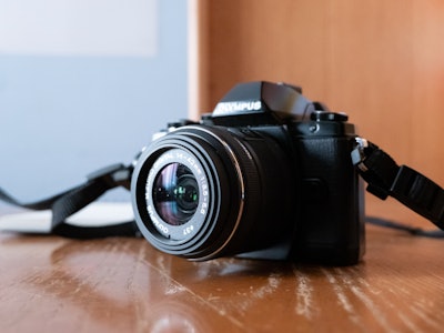 Camera on Desk - A black mirrorless camera with an attached lens on a wooden desk