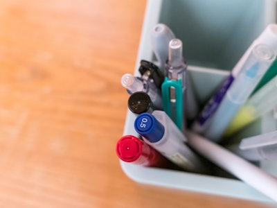 Pens on Desk - A group of pens and markers in focus sitting in a container on a wooden desk