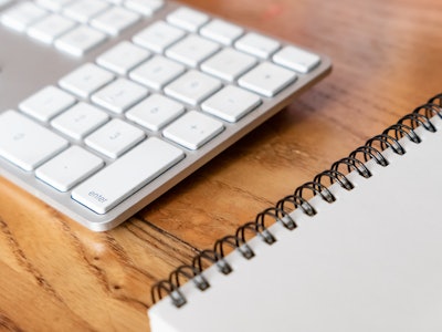 Keyboard and Notebook - A keyboard and notebook on a wooden desk 