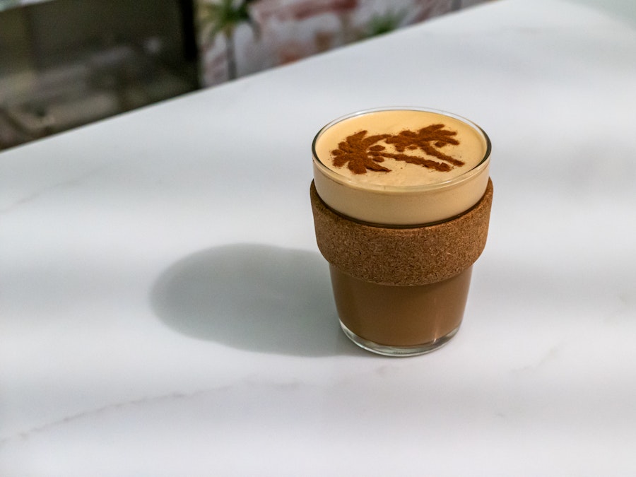 Photo: A glass with a foamy coffee latte drink and a palm tree design on top at a coffee shop