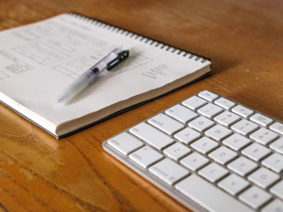Keyboard and Notebook - A keyboard, pen, and a notebook on a wooden table