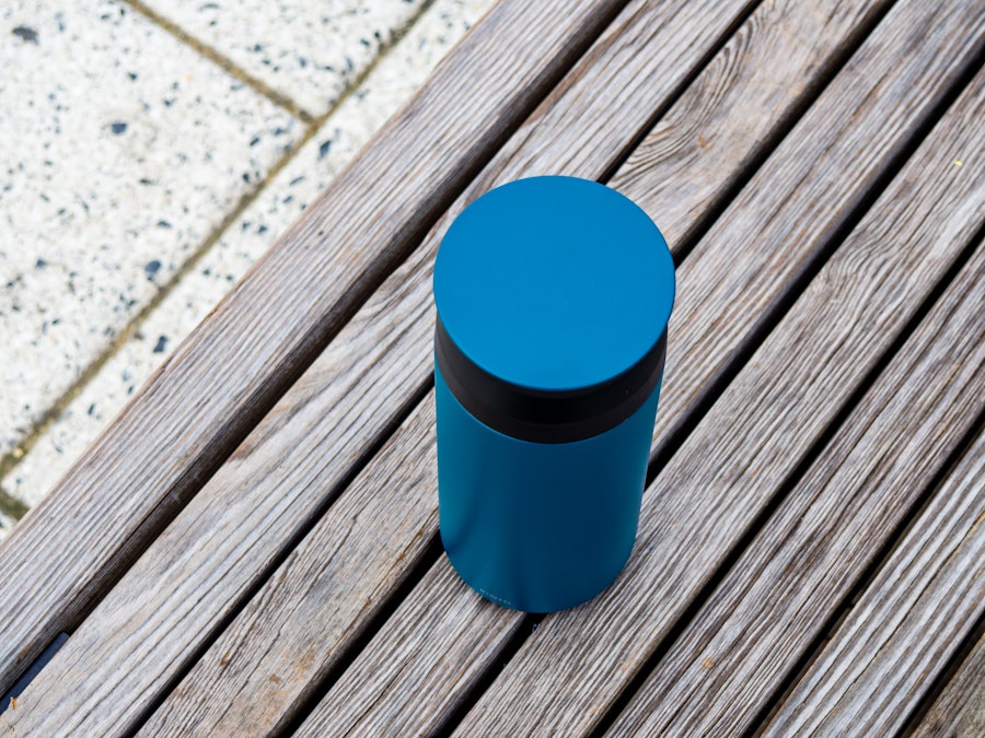 Photo: A blue coffee tumbler on a wood chair in a park