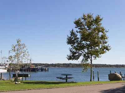 Park and Ocean - A road with grass and a bench in a park along a large body of water 