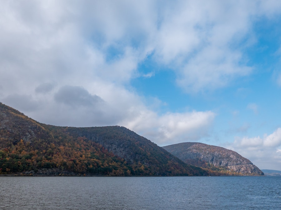 Photo: A body of water with a mountain range, hills, and trees under a blue sky