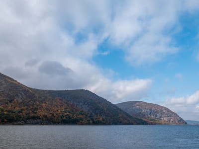 Mountains and Ocean - A body of water with a mountain range, hills, and trees under a blue sky