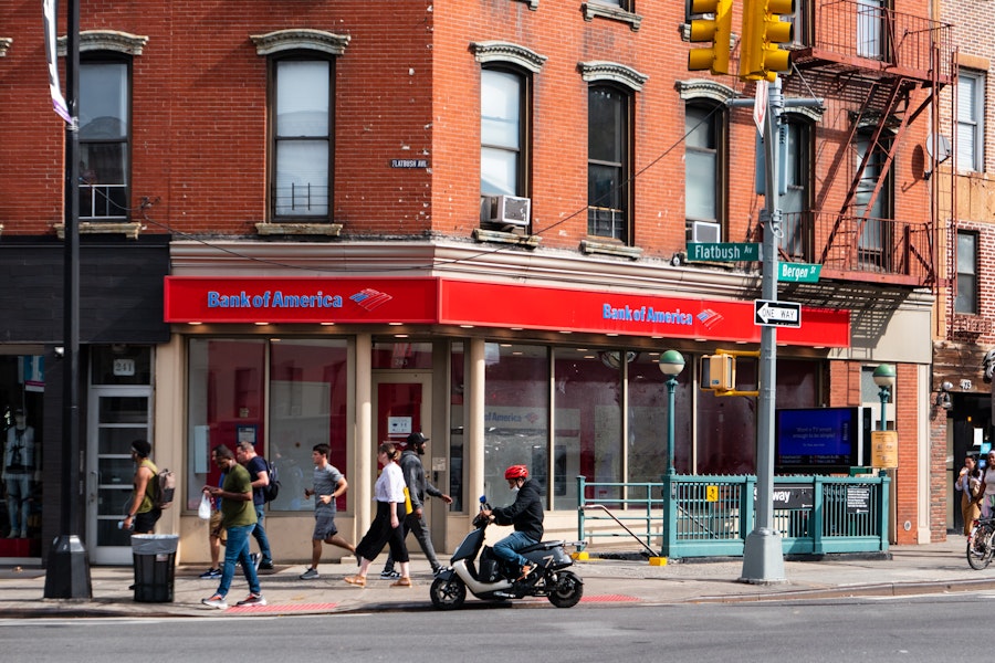 Photo: A group of people walking on a sidewalk surrounded by storefronts and apartment buildings 