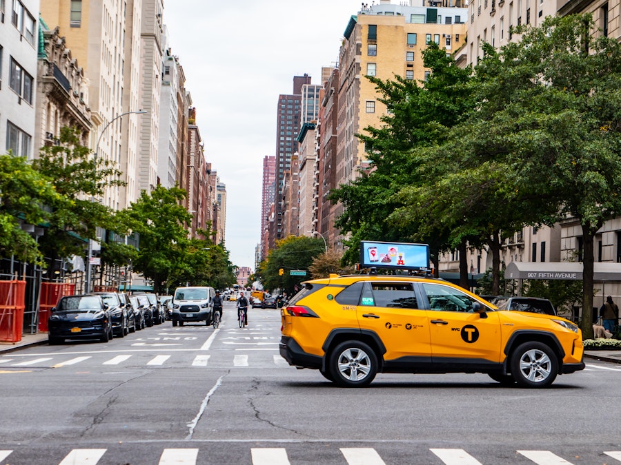 Photo: A yellow taxi, cyclists, and pedestrians on a city street