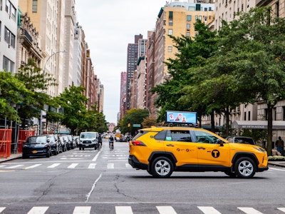 Taxi and Cyclist on Manhattan Street - A yellow taxi, cyclists, and pedestrians on a city street