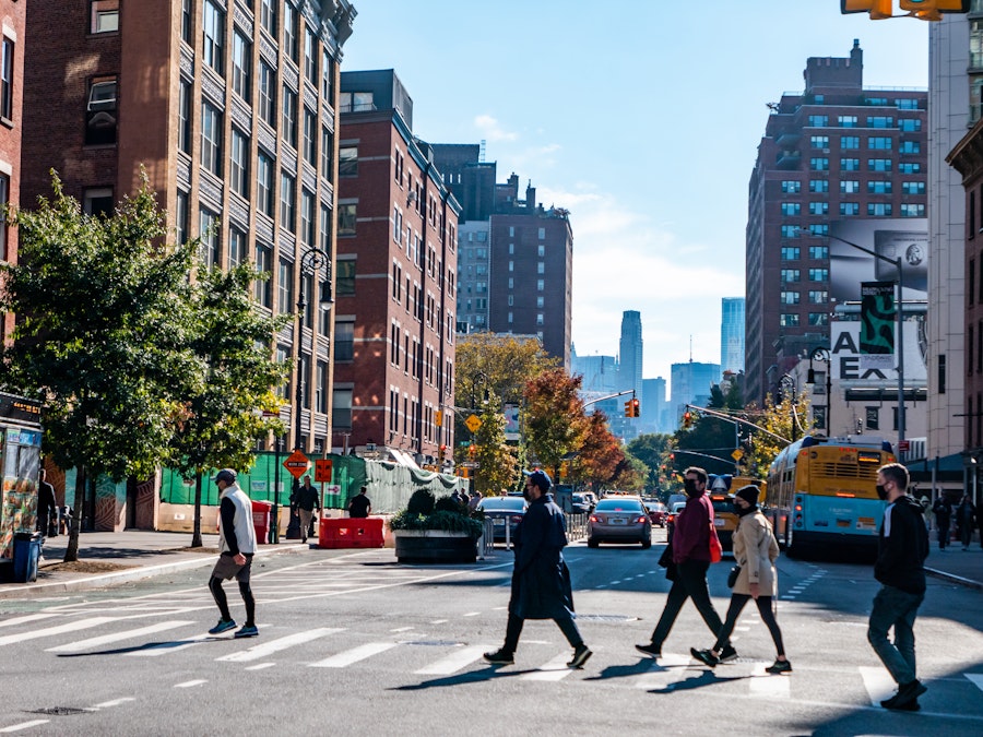 Photo: People crossing a street in a city with buildings, cars, and buses in the background 