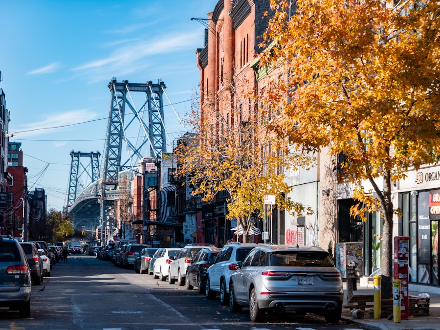 Photo: A city street with buildings, trees, and cars parked on it with a bridge in the distance