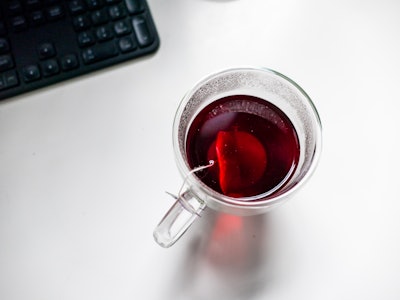 Hot Tea in Glass on White Desk - A cup of tea with a teabag in it on a white desk