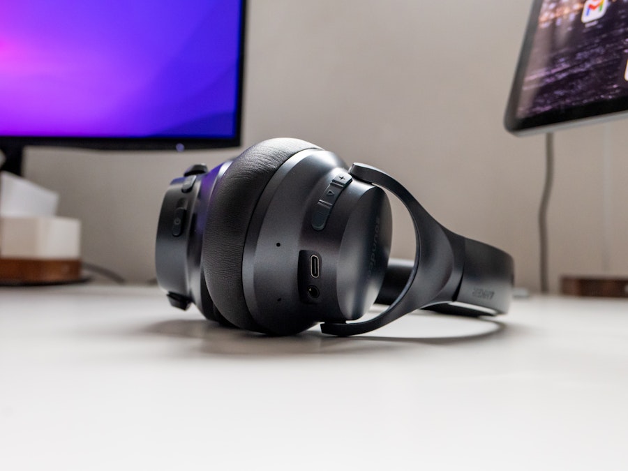 Photo: Black headphones on a white desk with a computer monitor in the background 