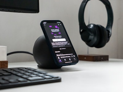 Desk with Headphones, Keyboard, and Phone on Charger - A smartphone on a wireless charger with headphones and keyboard in the background 