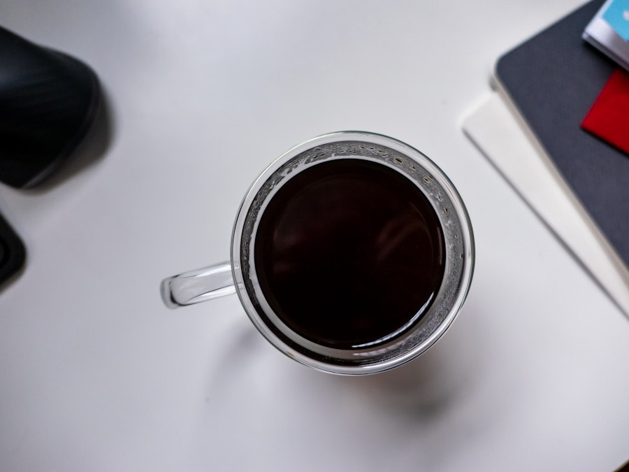 Photo: A cup of black coffee on a white desk with a blurred notebook in the background