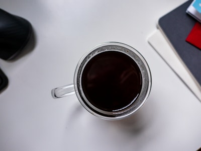 Coffee in Mug on White Desk - A cup of black coffee on a white desk with a blurred notebook in the background