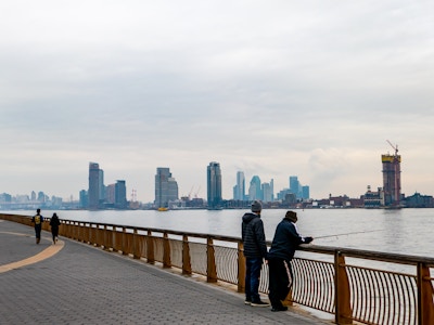 People Fishing in City Park - A group of people leaning on a railing overlooking a river in a park